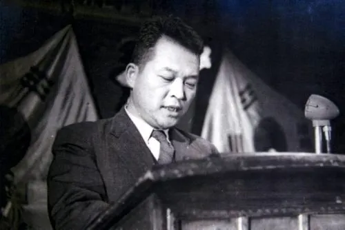 태극기 앞 연단에서 원고를 읽는 김원봉의 흑백 사진