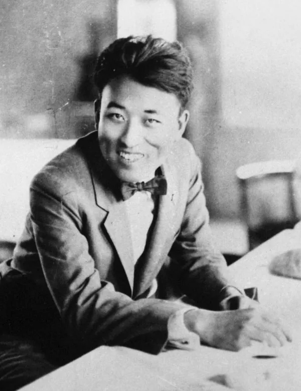 양복 차림의 남자가 책상에 기대 앉은 흑백 사진