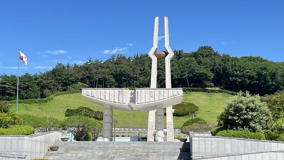 푸른 하늘 아래 두 기둥이 솟은 흰 추모탑과 넓은 광장