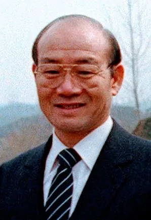 안경을 쓰고 양복에 넥타이를 맨 노년 남성이 웃고 있는 사진